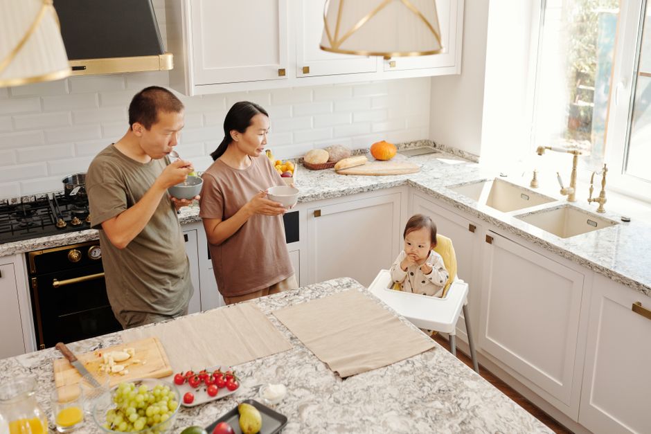 Asian family having breakfast together in a cozy kitchen. Parents and toddler in a high chair.